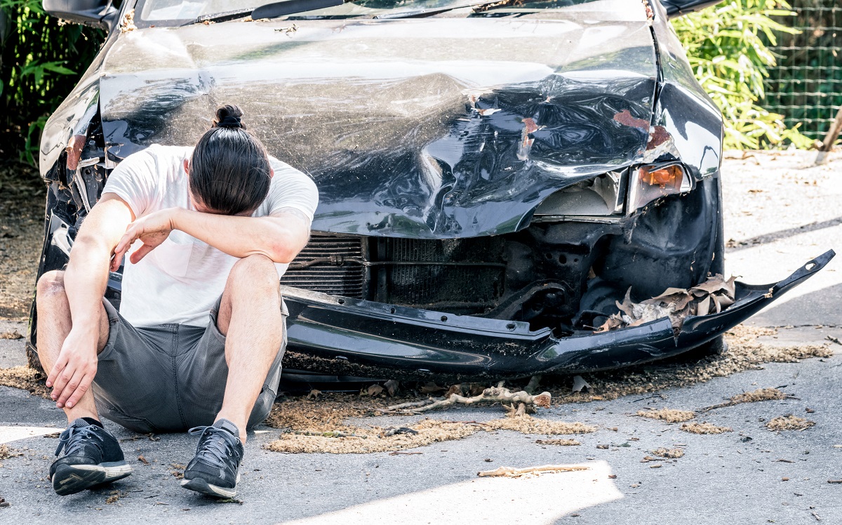 A man sitting in front of a car after a head-on car accident.
