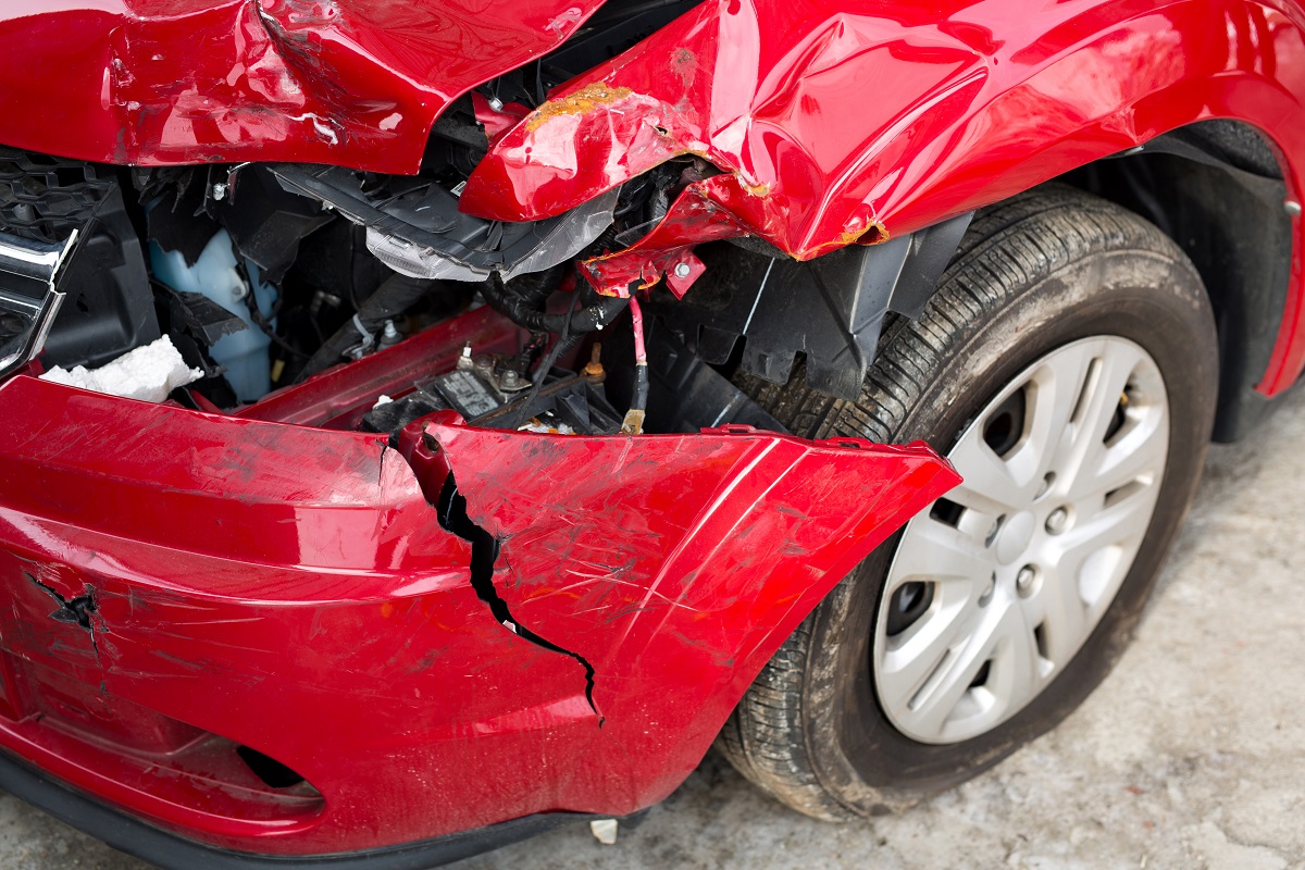 A damaged front fender and light on a red car.