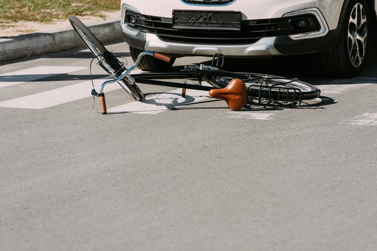 A bike on its side on the ground in front of a light-colored vehicle