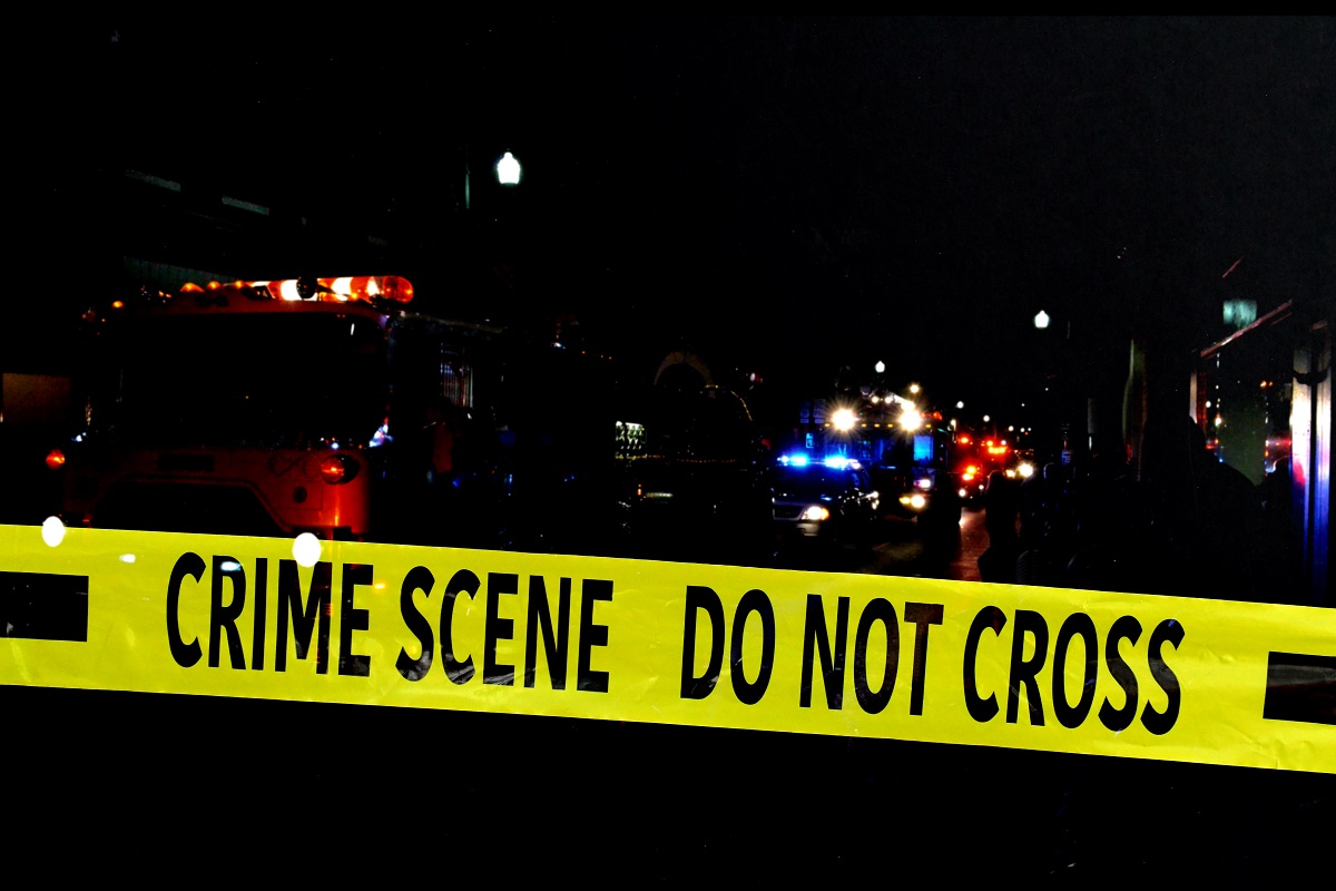 Yellow crime scene tape blocks off emergency vehicles with lights on at night.