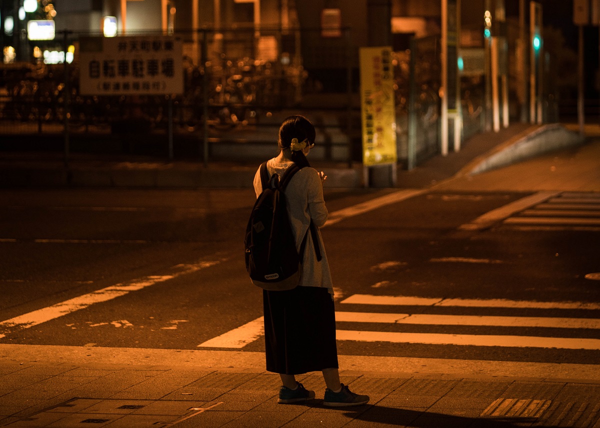 A pedestrian wearing a backpack crosses a road at night.