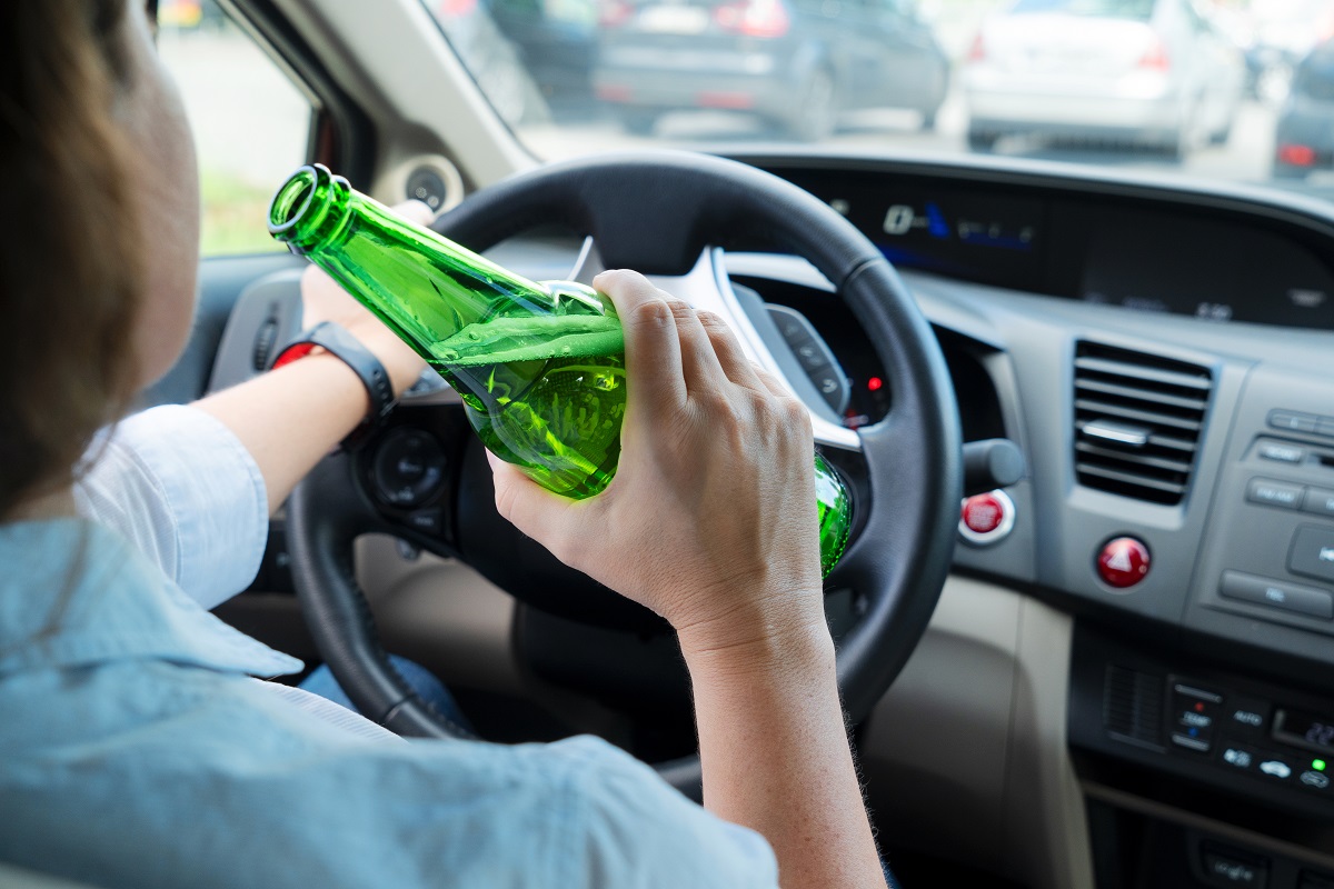 A woman drinking beer from a bottle while driving.