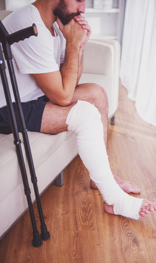 An injured man with crutches and one leg in a medical wrap.