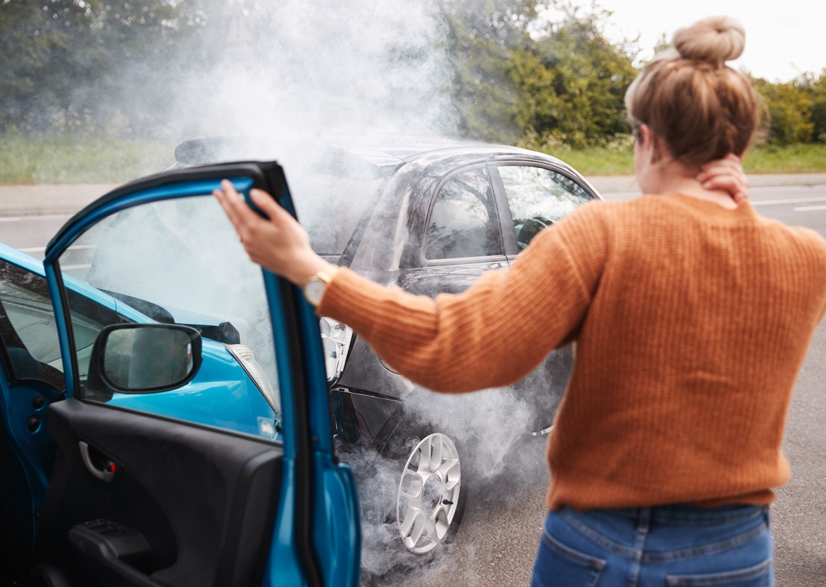 A woman standing outside the passenger side of a car following a rear-end collision.