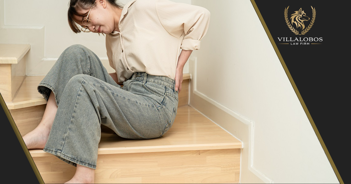 A woman sitting in a stairwell holding her back in pain after a fall.