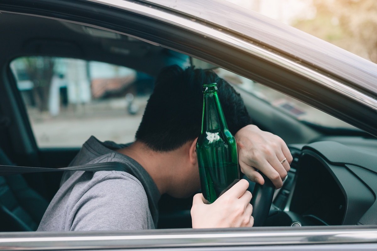 A driver in a car holding a green bottle of beer